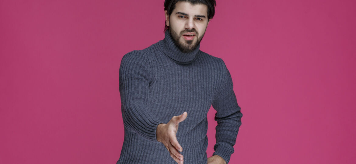 Man in grey sweater introducing or greeting someone with high energy and enthusiasm
