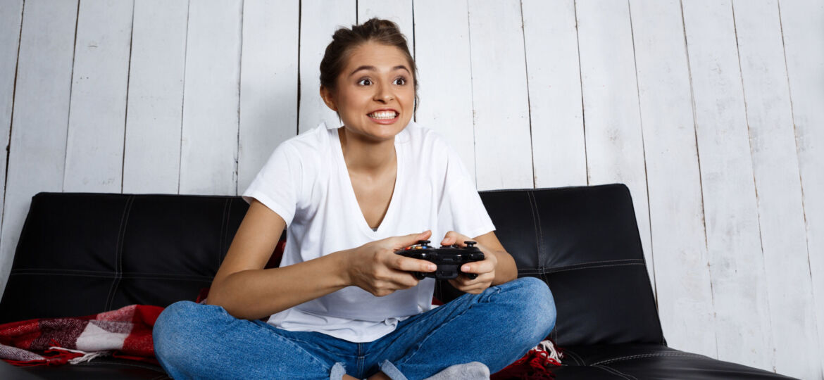 Beautiful girl playing video games, sitting on sofa at home.