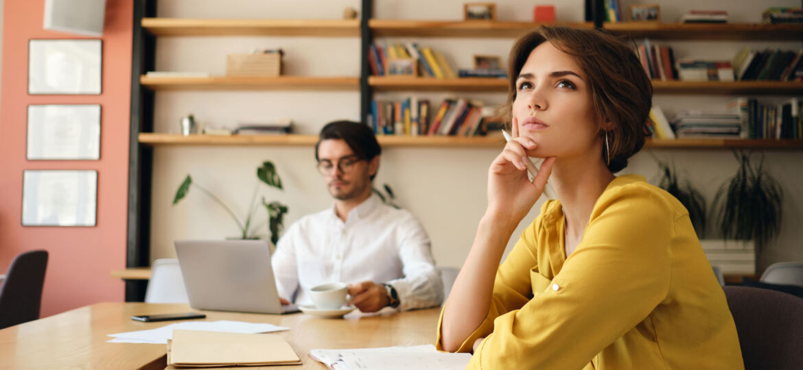 Young pensive woman sitting at the table with notepad dreamily l