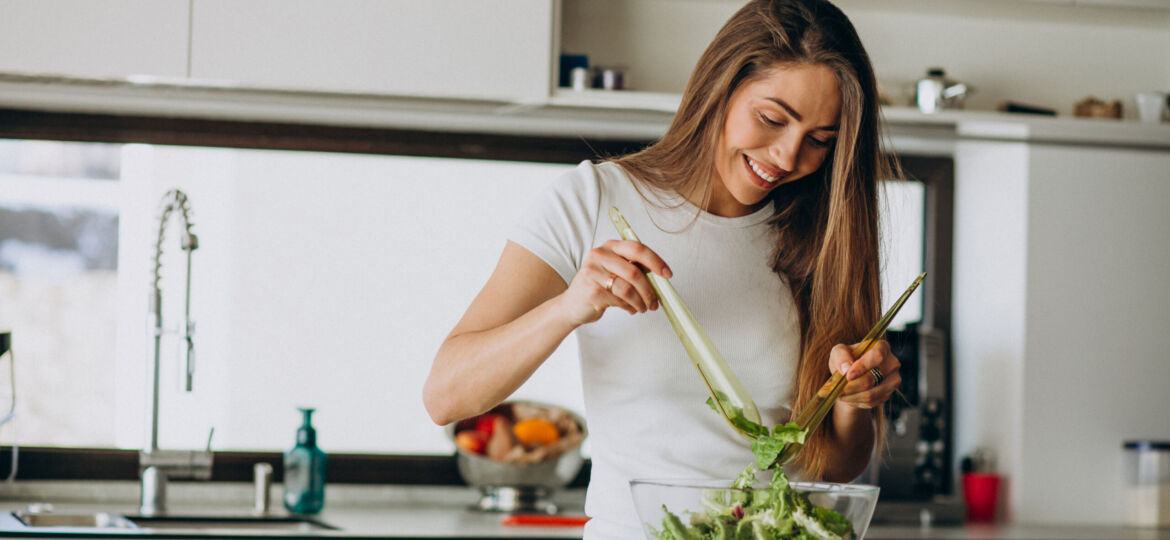 Young woman making salad at the kitchen