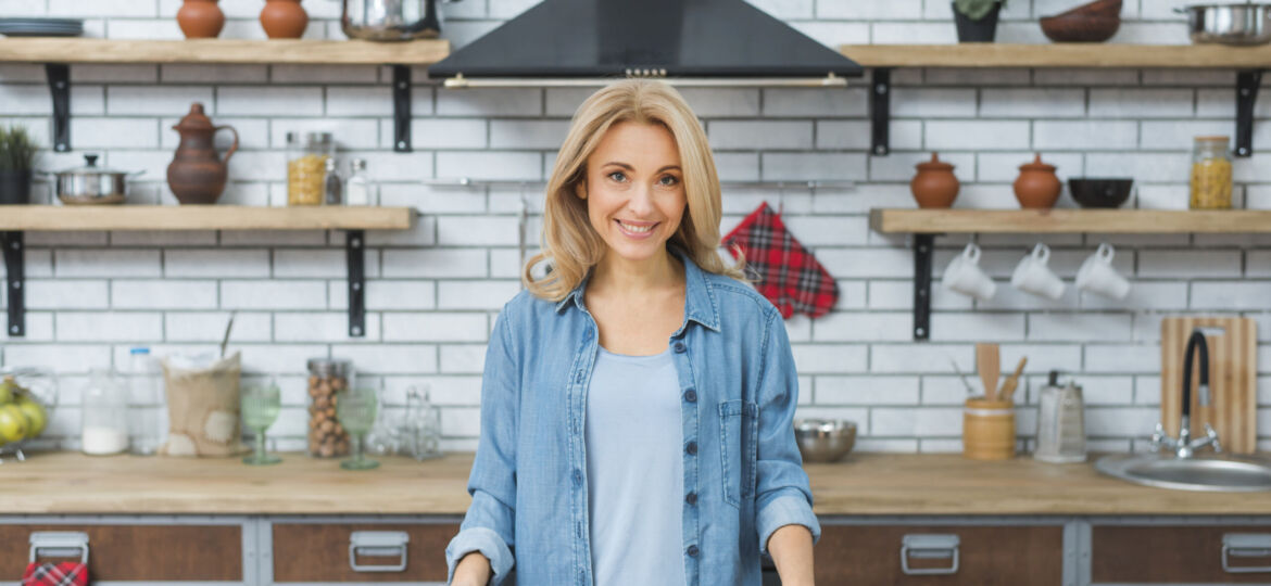 smiling-young-woman-standing-wooden-table-kitchen