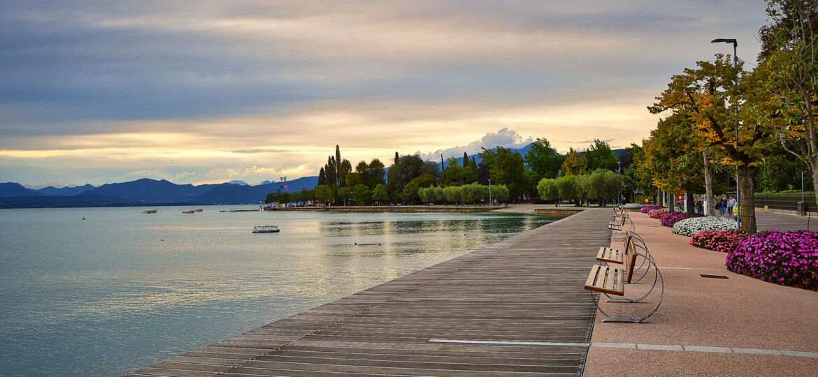 promenade pier of Bardolino, lake Garda with benches, flowers, trees, water and dramatic evening sky