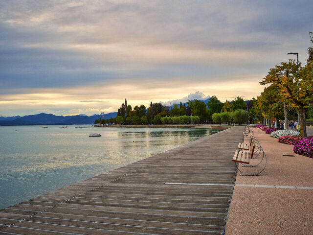 promenade pier of Bardolino, lake Garda with benches, flowers, trees, water and dramatic evening sky