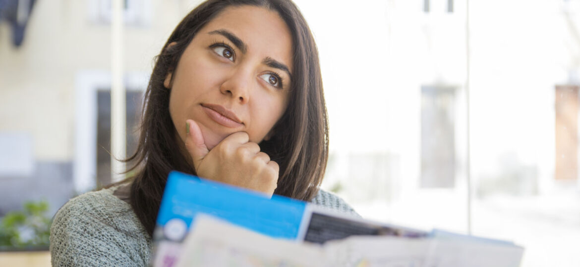 Dreamy pretty young woman using paper map in cafe