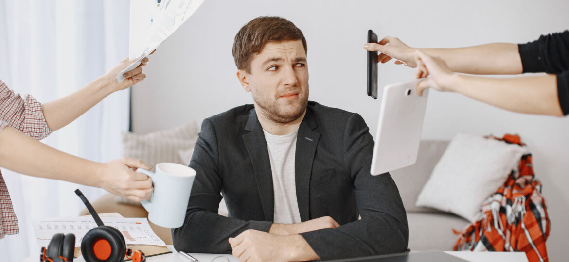 Many hands reach out to a man with various objects