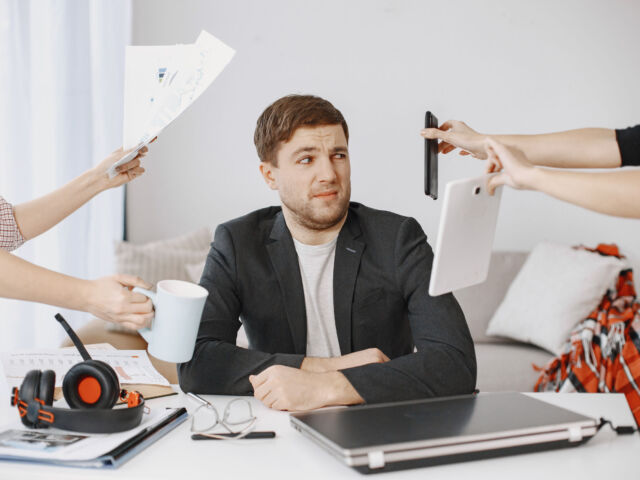 Many hands reach out to a man with various objects