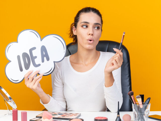 surprised-pretty-caucasian-woman-sitting-table-with-makeup-tools-holding-idea-bubble-looking-makeup-brush