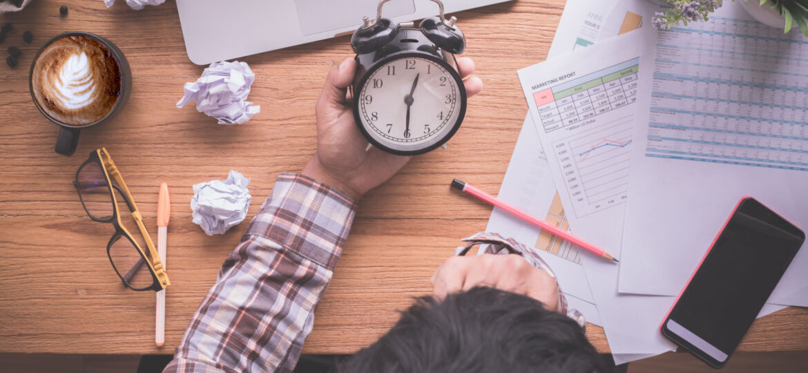 wood-table-with-businessman-holding-alarm-clock-late-payment-view-from-office-table