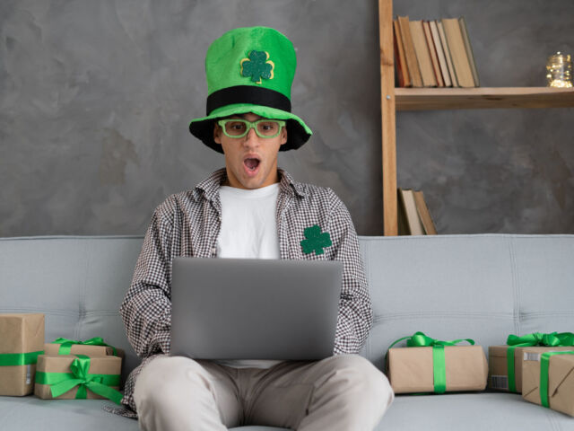 Young arabic man holding laptop scared and amazed with open mouth for surprise, disbelief face at home. St Patricks day online shopping